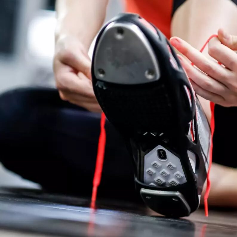 An adult dancer lacing up a tap shoe before class